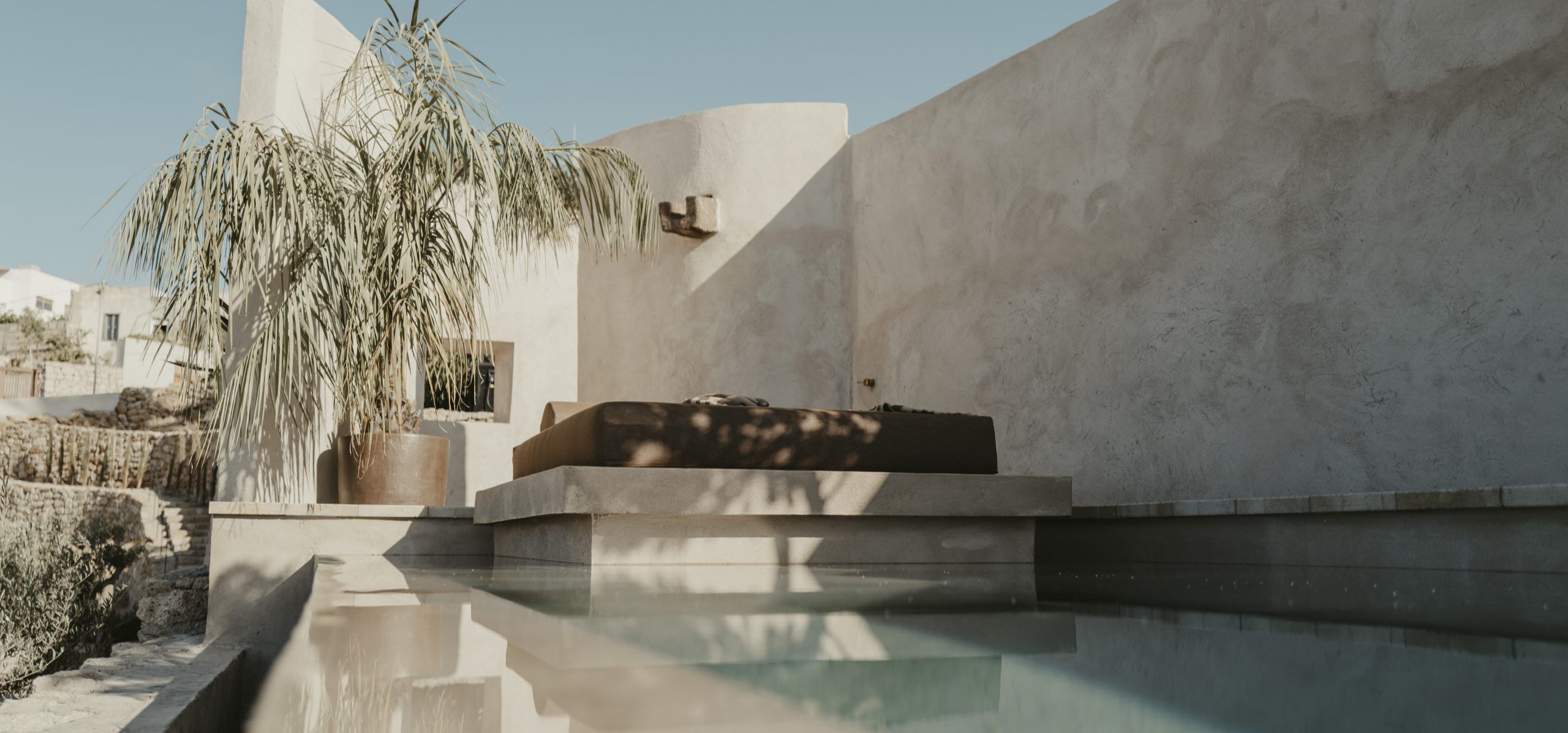 Zonovergoten binnenplaats met een plonsbad, een palm in pot en een daybed tegen witgekalkte muren
