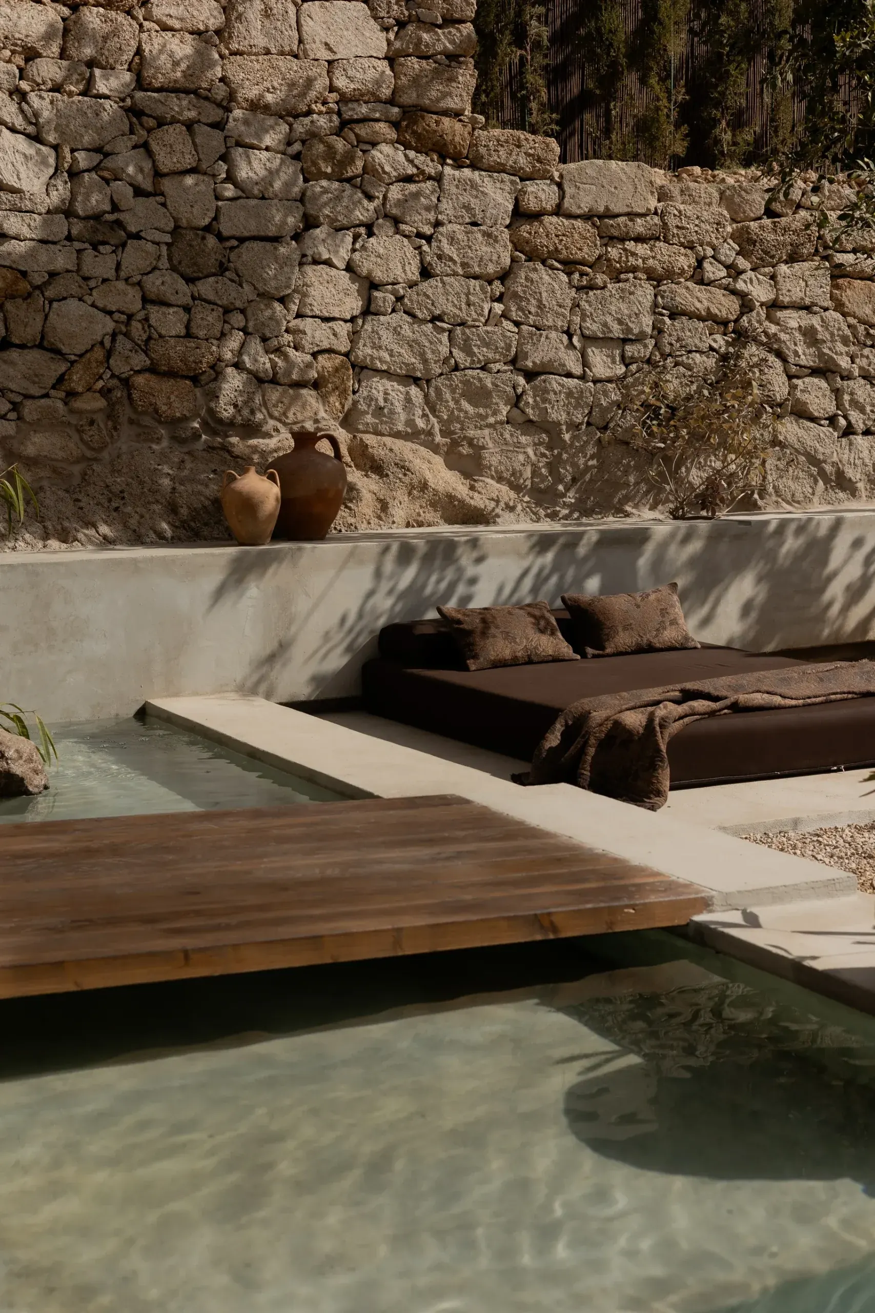 Buitenlounge met stenen muur, terracotta potten en een daybed